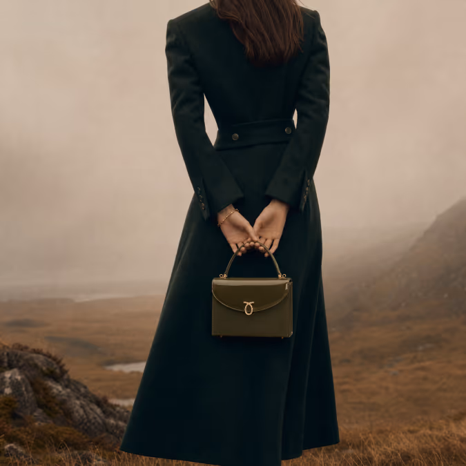 Fashion campaign image of a woman holding a handbag in a landscape